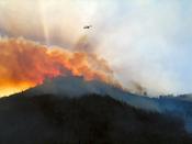 Wildfire in mountains with helicopter above.